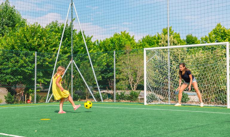 Mädchen schießt den Ball auf eine Frau im Tor auf einem Fußballplatz.