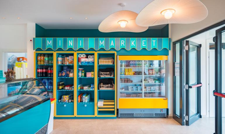 Mini market colorato con scaffali pieni di prodotti e frigorifero.