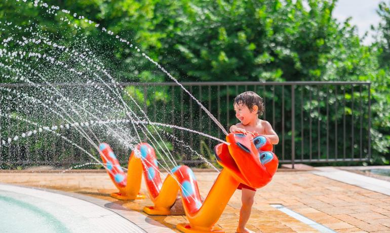 Kind spielt mit schlangenförmigem Brunnen am Pool.