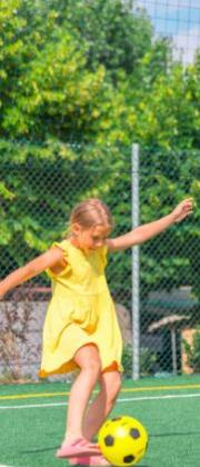 Girl in yellow plays soccer outdoors.