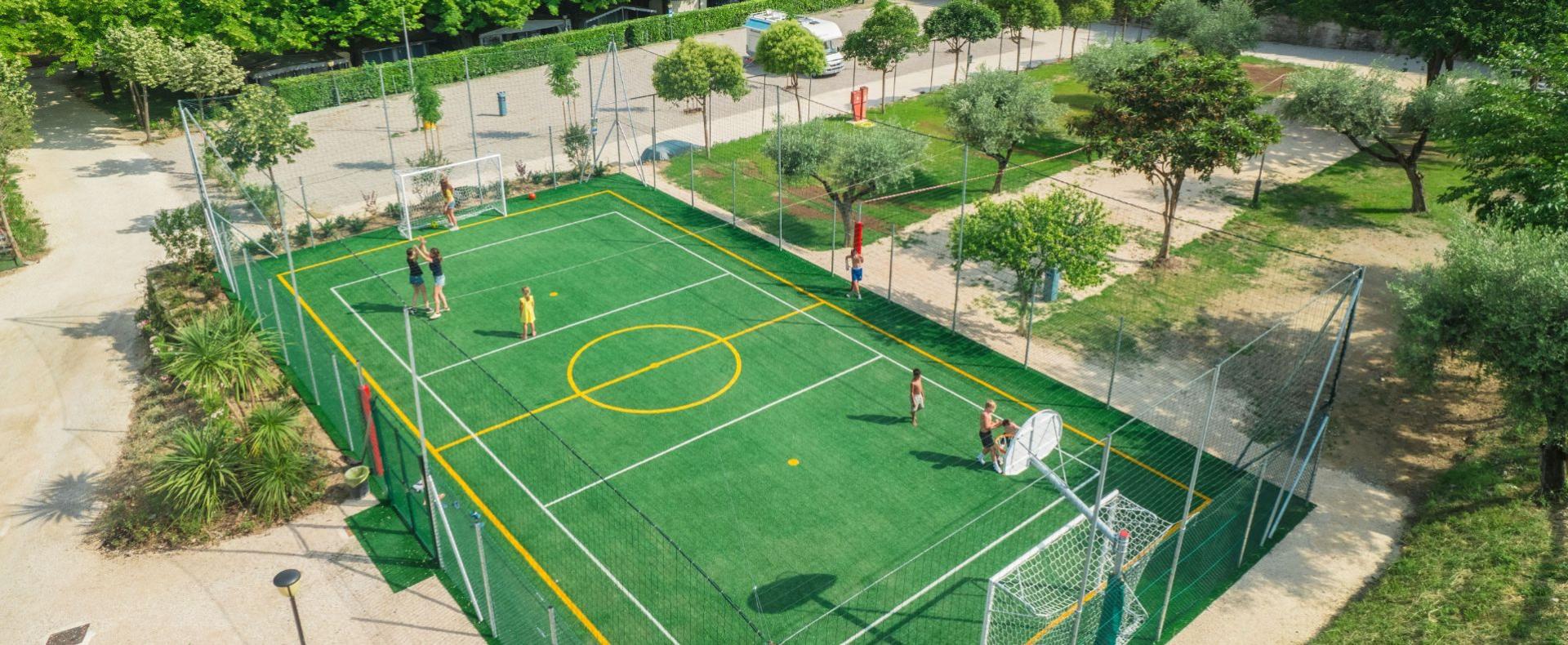 Outdoor sports field with people playing soccer and basketball.