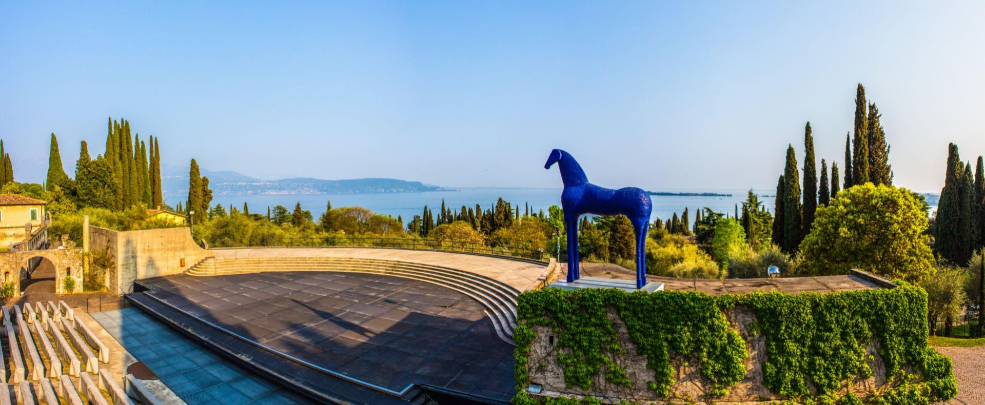 Amphitheater mit blauer Skulptur, Seeblick und Zypressen.