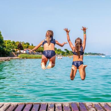 Two girls jump into the lake from a pier.