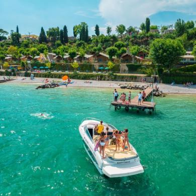 People on a boat near the beach with houses and trees in the background.