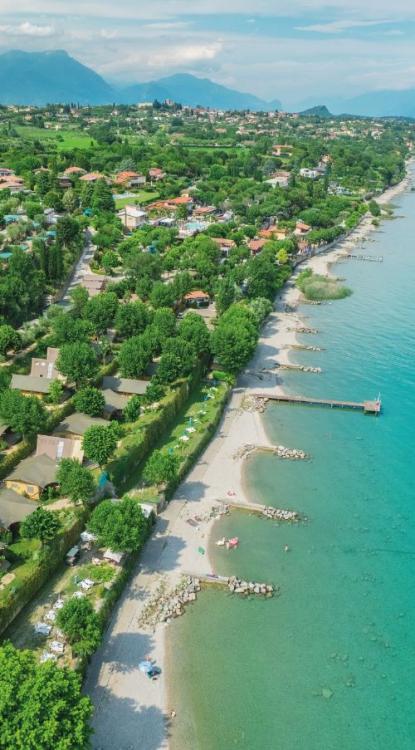 Ruhiger Strand mit kristallklarem Wasser und Häusern im Grünen.