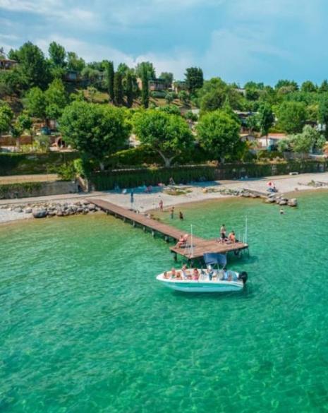 Beach with pier, boat, and people in crystal clear water.
