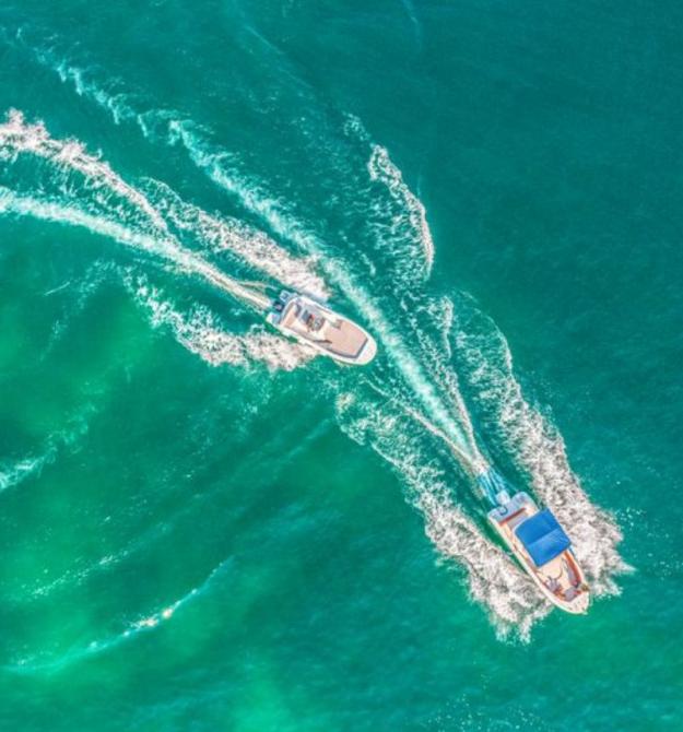 Two boats sail on crystal-clear waters, leaving white trails behind them.