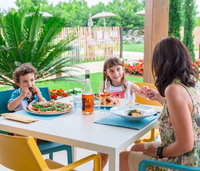 Family dining outdoors with pizza and wine, surrounded by greenery.