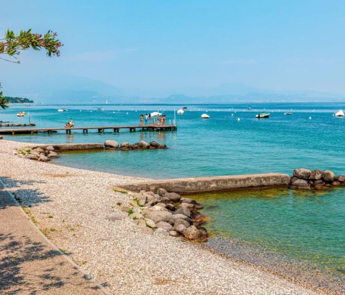 Pebble beach with pier, calm sea, and boats on the horizon.