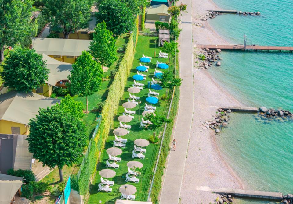 Beach with umbrellas and sunbeds near a green campsite.